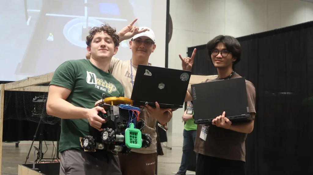 Three IEEE at USF students holding their SoutheastCon competition robot and laptops