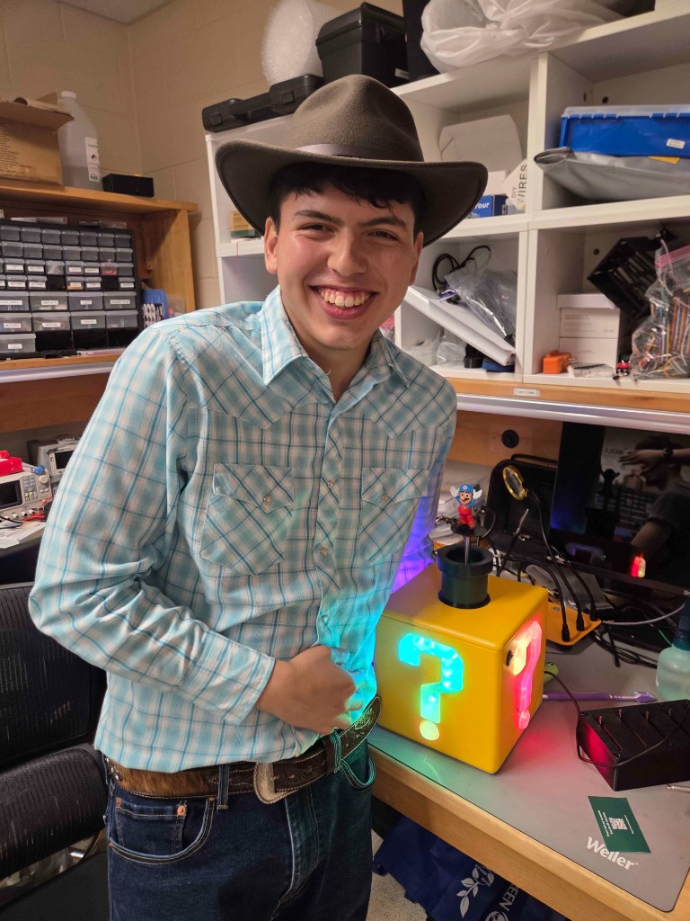 IEEE at USF member displaying an illuminated Mario question-block project during a lab session